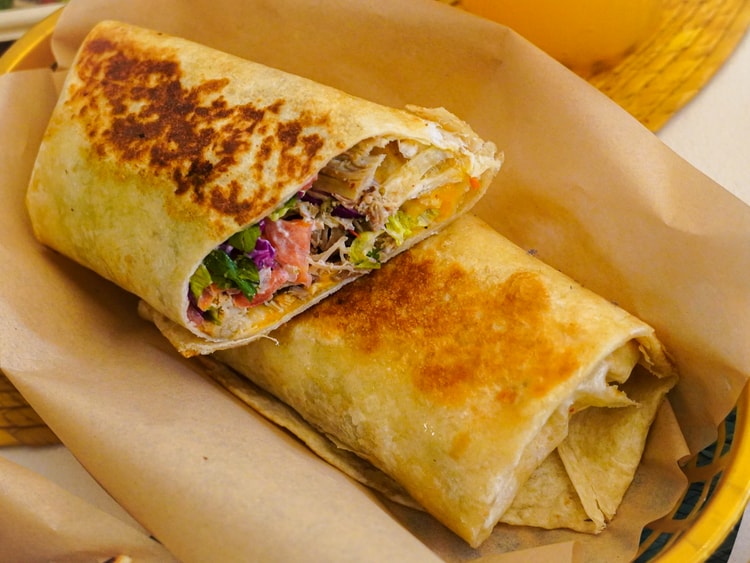 Wrap grillé ouvert, garni de légumes, sur une feuille de papier.
